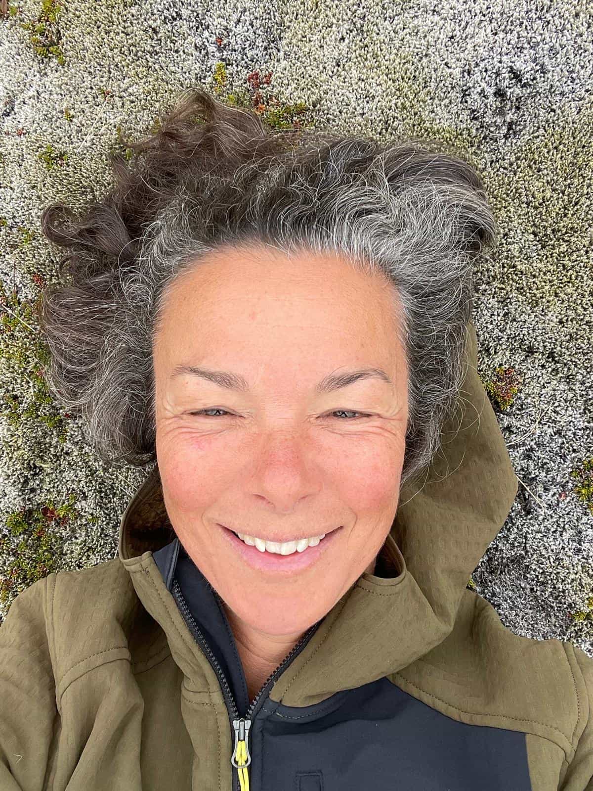 Caroline Tuchscherer smiles while lying in moss during a day outdoors.